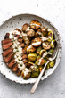 grilled steak alongside roasted potatoes & brussels accompanied with a horseradish cream sauce